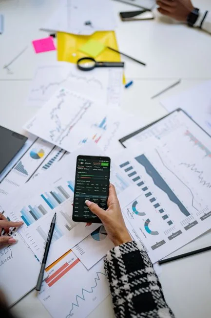 A sleek modern workspace where hands examine marketing data on a laptop alongside printed documents.